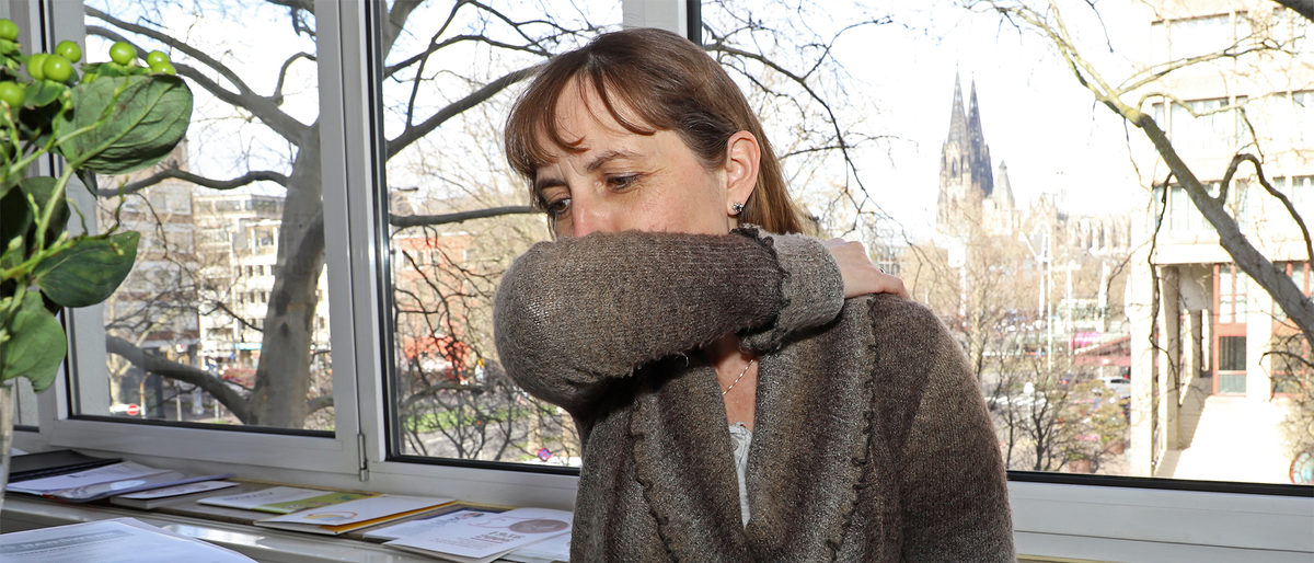Symbolbild: Aus gesundheitlicher Sicht ist es besser, sich in die Armbeuge zu husten, anstatt in die Hand. Unsere Kollegin zeigt, wie es geht. Frau hustet in die Armbeuge