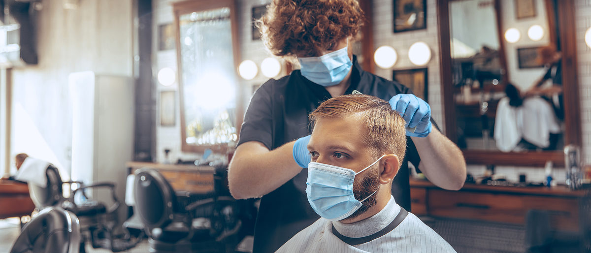 Man getting hair cut at the barbershop wearing mask during coronavirus pandemic. Professional barber wearing gloves. Covid-19, beauty, selfcare, style, healthcare and medicine concept. Schlagwort(e): man, barber, indoors, lifestyle, male, men, occupation, pandemic, people, professional, protected, protection, scissors, shave, short, small business, style, styling, treatment, trim, two, virus, hairstyle, working, hairdresser, grooming, hair, mask, haircut, salon, shop, head, service, barbershop, beauty, care, casual, comb, confinement, coronavirus, cosmetic, covid-19, customer, electric, equipment, gloves, hair care, hygiene, hipster, covid