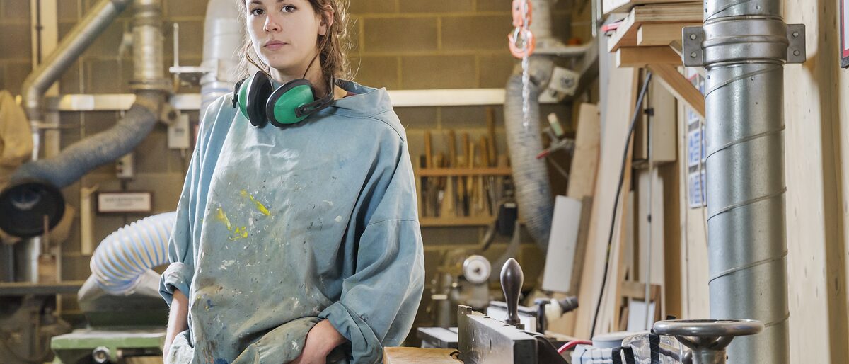 Portrait of young woman next to machinery in wood workshop Schlagwort(e): apprentice, apprentiship, art, artisan, carpenter, carpentry, colaboration, craft, creative, design, equipment, factory, graduate, hands on, industry, joiner, laborer, machinery, manufature, natural materials, overalls, post graduate, professional, project, protective wear, refinement, sanding, scholarship, small business, sole trader, studio, tangible, team, training, vison, woman, woodwork, working, workshop, young, young entrepreneur, industry, design, carpenter, apprentice, apprentiship, art, artisan, carpentry, colaboration, craft, creative, equipment, factory, graduate, hands on, joiner, laborer, machinery, manufature, natural materials, overalls, post graduate, professional, project, protective wear, refinement, sanding, scholarship, small business, sole trader, studio, tangible, team, training, vison, woman, woodwork, working, workshop, young, young entrepreneur