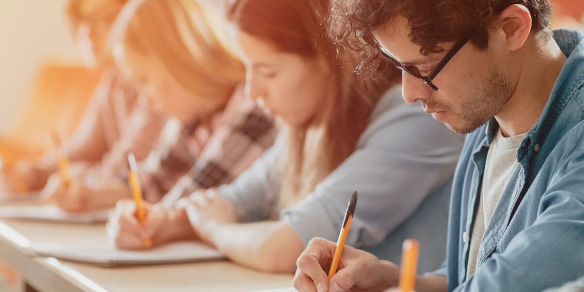Moving Footage of a Row of Multi Ethnic Students in the Classroom Taking Exam/ Test. Focus on Holding Pens and Writing in Notebooks. Bright Young People Study at University. Schlagwort(e): Modern, academic, academy, adult, asian, auditorium, black, campus, caucasian, class, classroom, college, contemporary, course, desk, diversity, education, educational, exam, faculty, group, hispanic, indoors, institute, learning, lectern, lecture, lecture hall, lecturer, lesson, listening, mixed race, multi ethnic, notebook, notepad, pen, people, person, room, school, sitting, students, study, talking, teaching, test, university, woman, writing, young