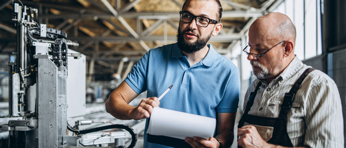 Young manager with beard showing and inspecting working process of adult professional worker on the big factory Schlagwort(e): equipment, standing, mechanic, machinery, discussing, workman, manufacture, cooperation, communicating, computer, employee, modern, technology, workplace, supervisor, expertise, two, quality control, professional, checking, working, uniform, control, management, indoors, production, warehouse, job, businessman, work, manufacturing, inspector, workshop, teamwork, talking, pointing, young, adult, male, people, worker, engineer, occupation, business, industrial, showing, man, industry, manager, factory