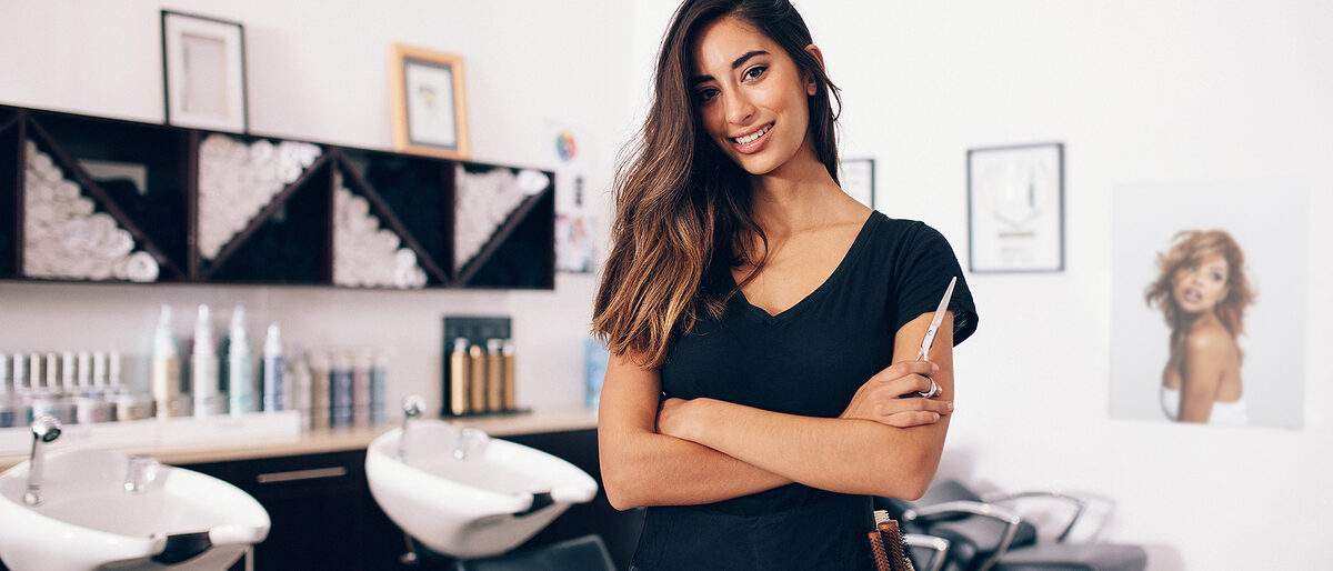 Female hairdresser in salon holding scissors in hand. Smiling young hairdresser standing in salon. Schlagwort(e): arms crossed, barber shop, beautician, beauty, beauty salon, business, dresser, equipment, expertise, fashion, female, hair, hair salon, hairdresser, hairstylist, holding, indoors, looking, mirror, occupation, parlor, portrait, professional, salon, scissors, smiling, staff, standing, studio, stylist, tool, woman, young